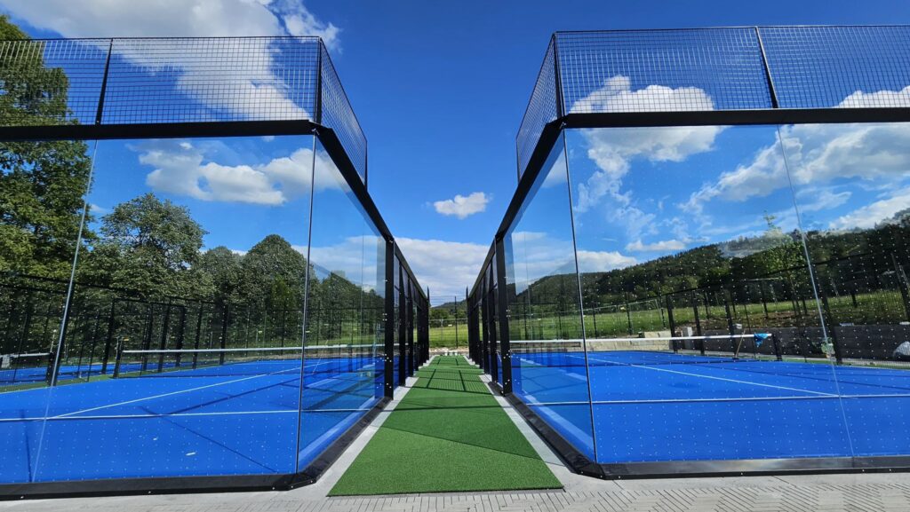 Moderne Padelplätze mit Glaswänden und blauem Bodenbelag im Alea Park Bad Orb, umgeben von grüner Landschaft und blauem Himmel.