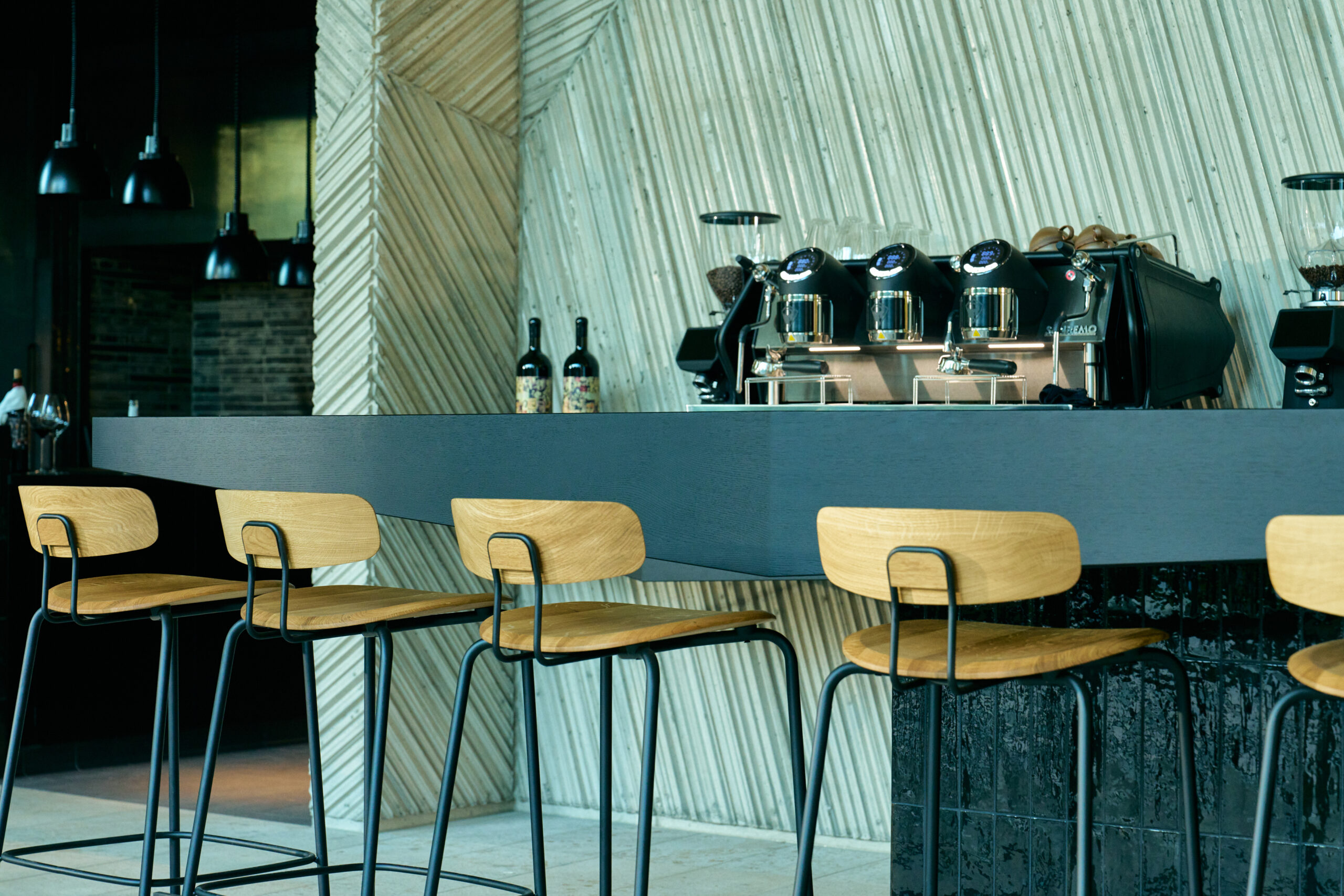 Moderne Kaffeebar mit hellen Holzbarhockern, Siebträgermaschine und strukturiertem Designinterieur