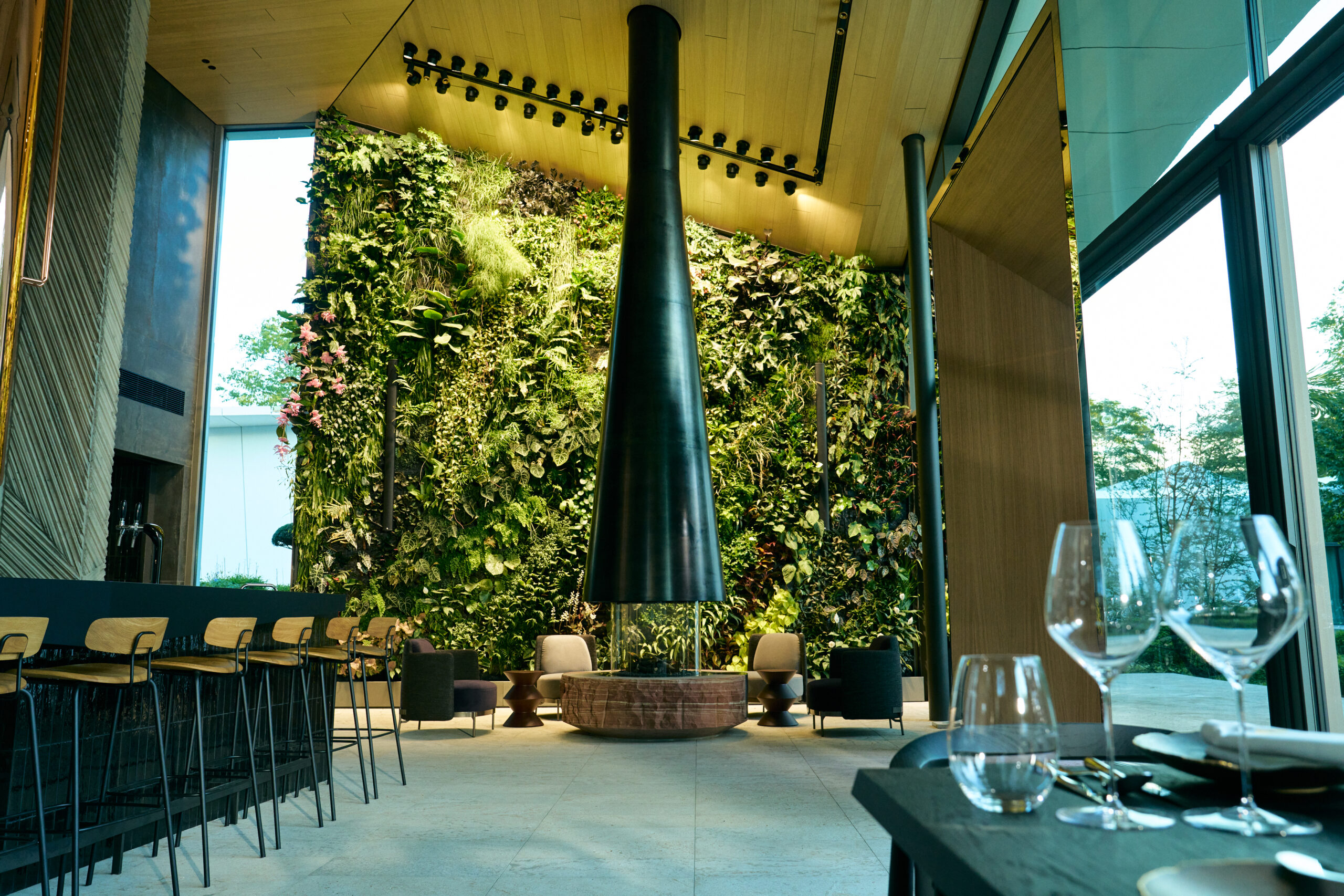 Design-Lounge im Alea Resort mit grüner Pflanzenwand, zentralem Kamin und moderner Bar – nachhaltiges Raumkonzept mit Naturbezug